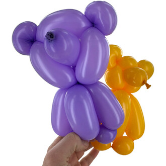 Deux ballons en forme d'animaux tenus par une main. Le ballon violet représente un ours avec des détails au niveau de la tête, tandis que le ballon orange prend la forme d'un petit animal. Les ballons sont colorés et brillants, créant un effet festif.