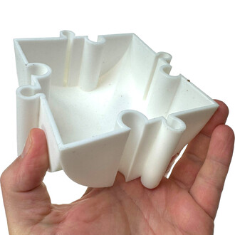 Intersections en plastique blanc pour poutres d'équilibre, tenues dans une main. L'objet présente une forme polygonale avec des courbes et des espaces pour emboîter les poutres.