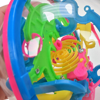 Boule de jonglerie transparente contenant un labyrinthe coloré en plastique avec des éléments verts, bleus, roses et jaunes, tenant dans une main.