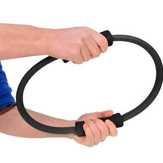 Main tenant un anneau de Pilates Sarneige, avec un design noir et des poignées en caoutchouc, sur fond blanc.