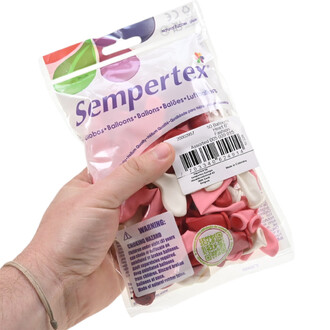Paquet transparent contenant un assortiment de ballons cœur rose et rouge de la marque Sempertex, tenu par une main, avec étiquette et code-barres visibles.