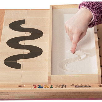 Enfant passant un doigt sur un tableau de sable, avec des blocs en bois présentant un motif en forme de vague, sur une surface en bois.