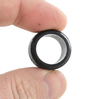 Gros plan sur une bague en caoutchouc noire Fusion tenue entre le pouce et l’index, surface extérieure texturée et intérieure argentée.