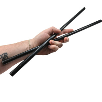 Trois baguettes noires brillantes de bâton du diable Gora tenues par une main sur fond blanc, avec un bracelet en corde au poignet.