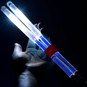 Baguettes de diabolo lumineuses tenues dans une main, avec des embouts lumineux et un design transparent. La lumière émise crée un effet visuel saisissant dans un fond sombre.