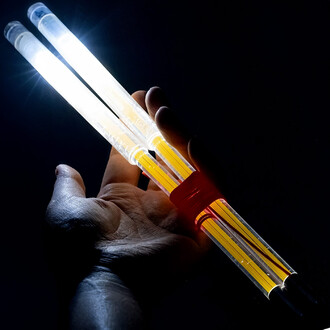 Baguettes de diabolo lumineuses tenues dans une main, avec des extrémités transparentes brillantes. La lumière éclaire les baguettes aux couleurs jaune et blanche sur un fond sombre.