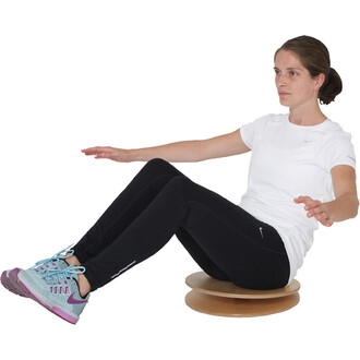 Femme assise sur un équilibre en bois, les bras tendus pour maintenir son équilibre, portant un t-shirt blanc et un pantalon noir, avec des chaussures de sport bleu clair et rose.