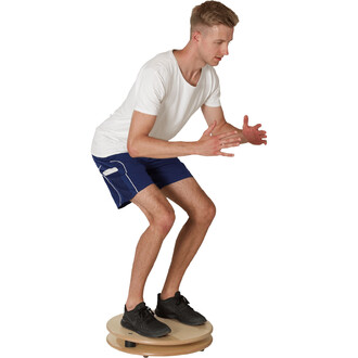 Homme équilibrant sur un plateau de jonglerie, vêtu d'un t-shirt blanc et de shorts bleus, en position de squat avec les bras tendus vers l'avant.