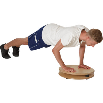 Un homme effectue un exercice de renforcement musculaire en position de planche sur un disque d'équilibre en bois. Il porte un t-shirt blanc et un short bleu. Ses mains sont posées sur le disque, tandis que ses jambes sont en extension derrière lui. Le fo