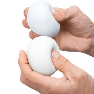 Deux balles de jonglage BBX Beanbag de Play sont tenues dans des mains. L'une des balles est blanche et l'autre est légèrement différente, montrant une texture de couture. Les doigts sont visibles en train de manipuler les balles, illustrant leur soupless