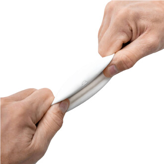 Deux mains tiennent une balle BBX Beanbag de Play, montrant la flexibilité et la texture du produit en l'étirant. La balle est principalement blanche avec un design lisse et ovale. L'arrière-plan est neutre, mettant en valeur le produit.