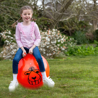 Enfant assis sur un ballon sauteur rétro dans un jardin, jouet d'extérieur amusant et résistant.