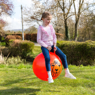 Enfant sautant sur un ballon sauteur rétro de 80cm dans un jardin, jouet d'extérieur amusant et résistant.