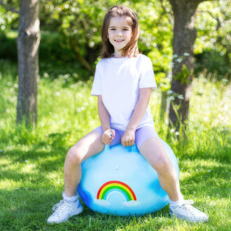 Enfant assis sur le ballon sauteur Tobar 60cm dans un jardin, souriant et tenant les poignées