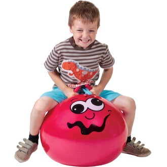 Enfant souriant assis sur un ballon sauteur junior rouge de 45 cm avec un visage souriant. L'enfant tient les poignées du ballon et semble prêt à sauter. Il porte un t-shirt rayé et un short bleu clair.