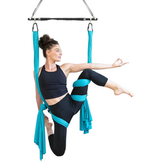 Femme pratiquant le yoga aérien suspendue à une barre de répartition noire Play, maintenant une posture avec des sangles turquoise.