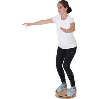 Femme en équilibre sur une planche de jonglerie, portant un t-shirt blanc et un legging noir, avec les bras tendus pour maintenir sa posture. Ses chaussures sont de couleur bleue avec des touches de rose.