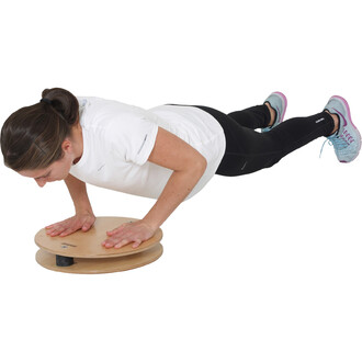 Femme en position de push-up sur un disque de jonglerie, vêtue d'un t-shirt blanc et de leggings noirs, avec des chaussures de sport. Elle effectue un exercice de renforcement musculaire, en se penchant en avant avec les mains sur le disque.