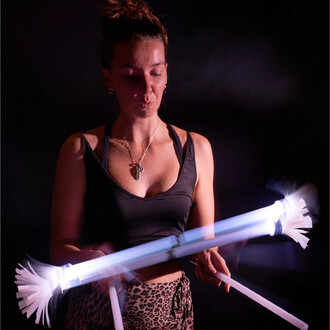 Femme en train de jongler avec des bâtons du diable lumineux, mettant en valeur la manipulation artistique des bâtons. L'éclairage met en avant les détails des bâtons, tandis que le fond est sombre pour accentuer l'effet lumineux.