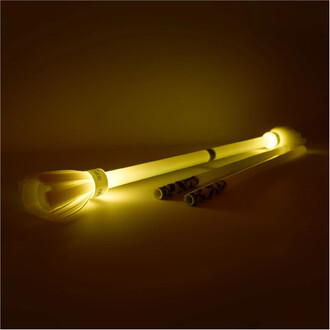 Baton du Diable Lumi Pro de Trickstix posé sur une surface claire, illuminé par une lumière jaune douce. Le bâton présente une pointe décorative et deux autres bâtons plus petits, tous dégageant une lueur lumineuse dans un environnement sombre.