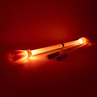 Baton du Diable Lumi Pro - Trickstix sur fond rouge, avec des embouts lumineux émettant une lumière orange, accompagné de deux bâtons supplémentaires.