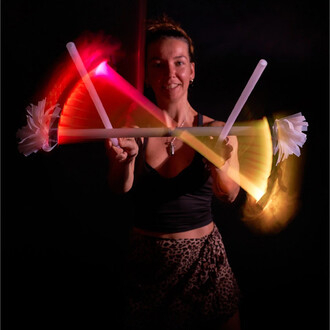 Femme tenant des bâtons du diable lumineux, en train de jongler avec des effets lumineux colorés en arrière-plan sur un fond noir. Elle porte un haut noir et une jupe à motif léopard.
