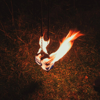 Bolas enflammées suspendues, avec des flammes vives et des chaînes, sur un sol herbeux. L'image met en avant l'effet spectaculaire du feu dans un environnement sombre.