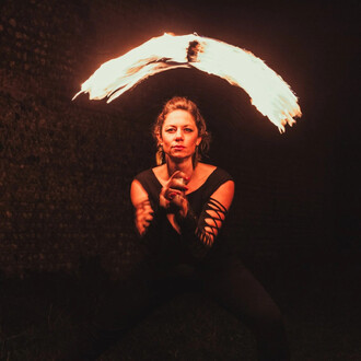 Femme effectuant un spectacle de jonglerie avec des bolas de feu, entourée d'une obscurité mettant en valeur la flamme en mouvement. Elle est vêtue d'un haut noir et dégage une concentration intense tout en manipulant les bolas.