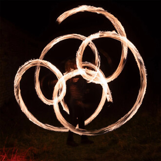 Spectacle de jonglage avec des bolas en feu, créant des spirales lumineuses dans l'obscurité. Le jongleur, silhouetté, manie les bolas avec habileté, générant des traînées de flammes brillantes.