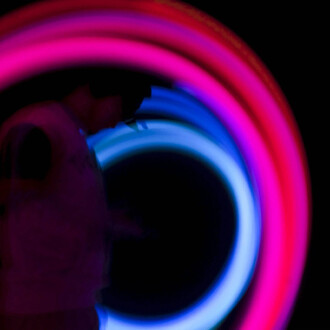 Gros plan sur des bolas LED Echo Orbit en mouvement, traînées lumineuses magenta et bleu dans l'obscurité, une main apparente à gauche.