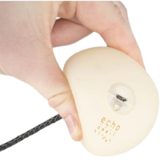 Bola LED Echo Orbit blanche tenue par une main avec cordon noir tressé et petit port/connecteur visible sur la surface.
