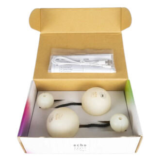 Boîte en carton ouverte contenant des bolas LED Echo Orbit blanches, un câble USB rangé dans un sachet et le manuel, emballage d’origine.