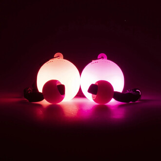 Bolas LED Echo Orbit de Firetoys, affichant deux grandes boules blanches lumineuses qui émettent une lumière rose ou violette, accompagnées de deux petites boules. Les bolas sont placées sur une surface sombre, créant un effet visuel captivant avec un écl