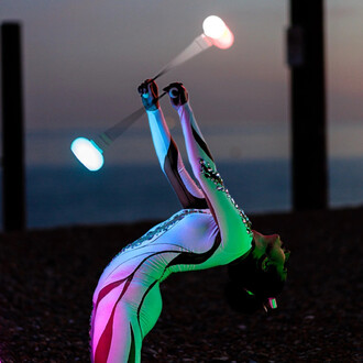 Artiste en train de jongler avec des bolas LED Echo Orbit, créant des effets lumineux colorés sur fond de coucher de soleil au bord de la mer. La personne est en position dynamique avec un costume aux motifs géométriques, accentuant l'élasticité et le mou