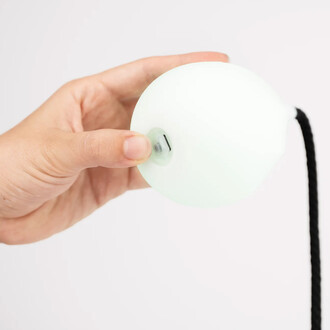 Main tenant une bola lumineuse Lumi Pro de ThreeWorlds, montrant la partie supérieure du produit avec un design rond et translucide, tandis qu'un cordon noir est visible à l'arrière.