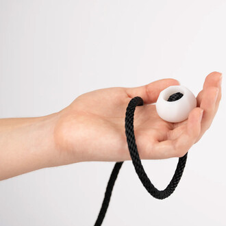 Bola lumineuse Lumi Pro dans une main, avec une corde noire enroulée. Le bola est de couleur blanche et possède une ouverture au centre. Fond blanc.