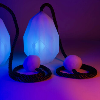 Bolas lumineuses USB Prism de Threeworlds, avec des têtes en forme de diamant diffusant une lumière bleu-violet, attachées à un cordon noir, sur un fond aux dégradés de couleurs.