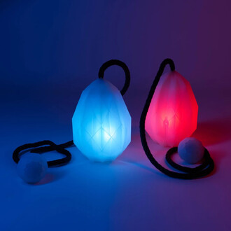 Bolas lumineuses en deux couleurs, avec un modèle en forme de diamant, une bleu et une rouge, reliées par une corde noire. Un petit bol en plastique blanc est également présent au premier plan sur un fond dégradé de bleu à violet.