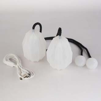 Bolas lumineuses USB Prism avec deux boules en silicone translucide, de forme facettée, attachées par des cordes noires et accompagnées d'un câble de charge USB.