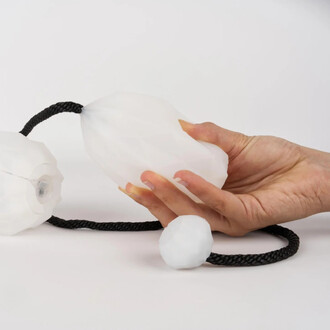 Une main tient une des bolas lumineuses USB Prism, qui est de forme octogonale avec une texture en relief. L'autre bola est posé sur une surface blanche, relié par une corde noire. L'arrière-plan est également blanc, mettant en valeur le produit.