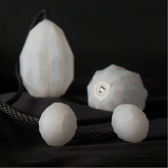 Bolas lumineuses USB Prism de Threeworlds, composées de deux bolas en forme de diamant et une coque de protection blanche, avec une corde noire. Les bolas présentent un design géométrique et sont placées sur un fond noir.
