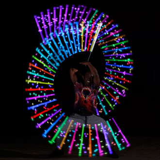 Un jongleur exécutant des figures avec des bolas lumineuses de 31 cm, créant un effet de lumière coloré en cercle sur fond noir. Il porte un t-shirt aux motifs galactiques et dégage une expression joyeuse.