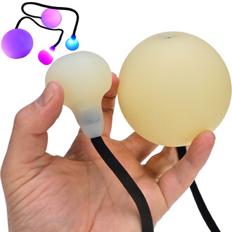 Main tenant deux bolas lumineuses Supernova, une grande et une petite, avec un cordon noir. Les bolas sont partiellement transparentes et émettent des lumières colorées. En arrière-plan, d'autres bolas lumineuses dans des teintes violettes et bleues.