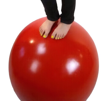 Une personne se tient debout sur une boule d'équilibre rouge de 70 cm de diamètre, montrant ses pieds nus avec des ongles de pieds peints en jaune.