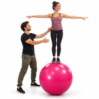 Donna in equilibrio su una palla da equilibrio rosa di 70 cm, con le braccia tese, assistita da un uomo che la guida, su sfondo bianco.