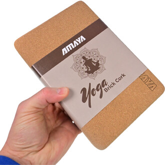 Brique de yoga en liège tenue à la main, avec un design épuré. La brique présente une surface supérieure en liège naturel et un emballage avec le logo AMAYA et le texte Yoga Brick Cork sur fond beige.