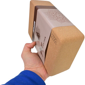 Brique de yoga en liège Sarneige tenue à la main, montrant une surface en liège naturel et un emballage élégant avec un design graphique sur le côté.