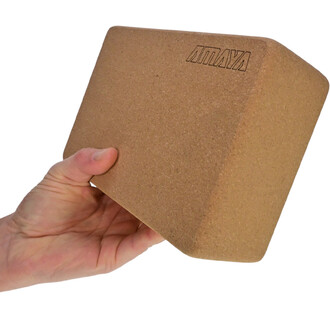 Brique de yoga en liège, tenue à la main, avec une surface lisse et un logo marqué en haut.