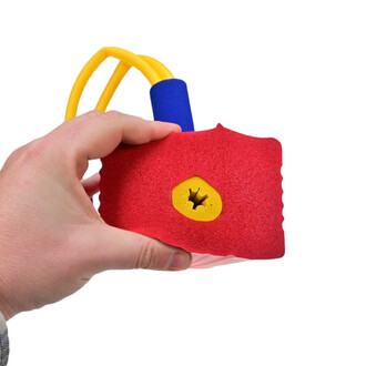 Main tenant un dispositif Bungee Sauteur avec un corps rouge en mousse. Ce dernier présente un trou jaune en forme d'étoile. Un tube bleu et des cordes jaunes sont visibles, suggérant un système de saut et de rebond. Fonds blanc.