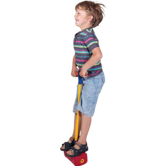 Enfant souriant utilisant un Bungee Sauteur, debout sur une base rouge, tenant les poignées avec des cordes jaunes et bleues. Il porte un t-shirt rayé et un short en jean.